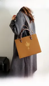Detail of a brown leather tote bag with gold crown logo worn over a grey coat