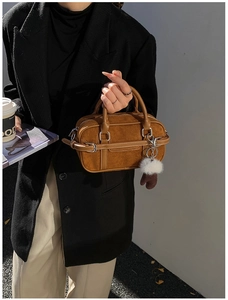 Close-up of brown suede bowling bag with contrast stitching and a white fur charm