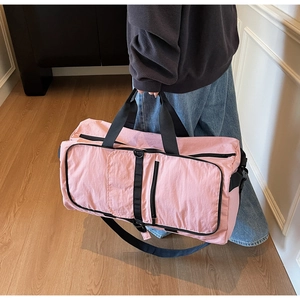 Lifestyle view of a pink nylon travel bag with black straps on a wooden floor
