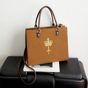 Macro detail of brown frosted leather handbag with golden crown and sword emblem