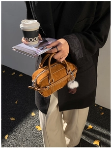Detail of brown suede bowling bag with white stitching and plush glove charm accessory