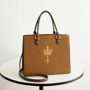 Brown leather tote bag with gold crown emblem and adjustable shoulder strap for daily use