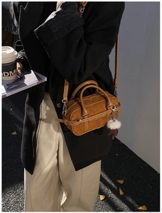 Close-up of brown suede bowling bag with dual handles and a decorative white fur ball charm