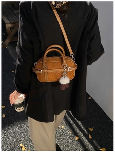 Close-up of brown suede bowling bag styled with a black coat and plush pendant