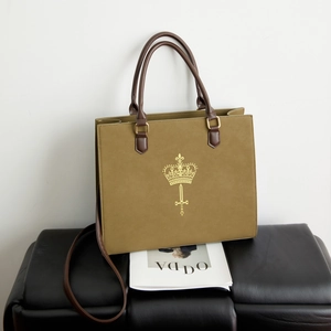 Detailed view of olive green tote bag with gold crown print and brown handles on leather bench