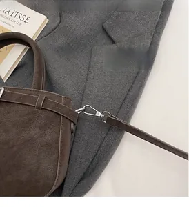 Détail du crochet métallique argenté et texture cuir sur le sac seau marron foncé