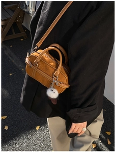 Close-up of brown suede bowling bag featuring a white fuzzy pompom charm detail