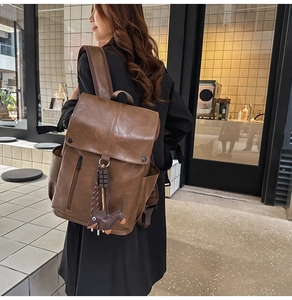 Brown vintage faux leather backpack with dog charm worn by woman on modern street