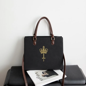 Detail of black leather square tote featuring gold crown motif and brown handles