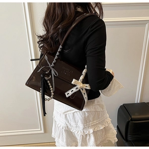 Detail of dark brown patent leather shoulder bag with lace bow and pearl chain