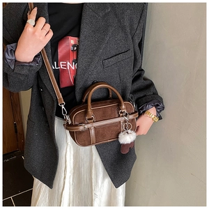 Close-up of brown suede bowling bag featuring a soft pom-pom charm and leather strap