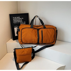 Detail view of orange travel duffel bag set with matching crossbody bag on a display stand