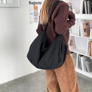 Large black nylon crescent hobo bag shown worn on shoulder in a cozy studio