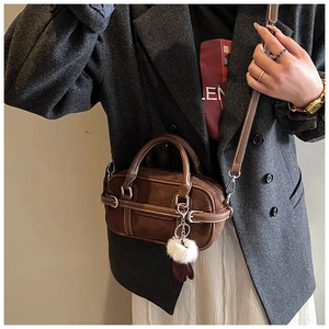 Detailed close-up of brown suede mini bowling bag with strap and plush ball charm
