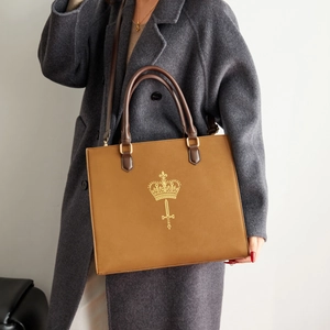 Large brown tote bag with gold crown logo on grey wool coat shown by model