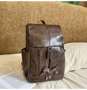 Detail of vintage brown PU leather backpack with a dog pendant in a cozy home setting