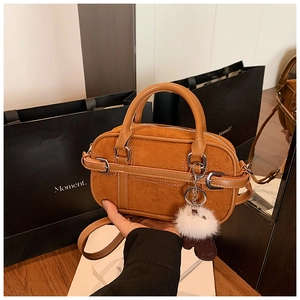 Detail of caramel suede leather handbag with metal buckle and soft white fur ball charm
