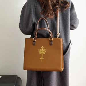 Brown leather tote bag with gold crown logo worn over a dark grey wool coat