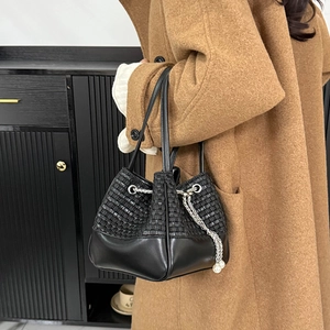 Détail du sac seau noir tressé avec finitions en cuir et accents de perles sur cordon