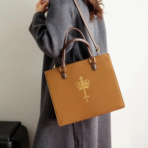 Macro view of vintage brown tote bag with gold crown emblem and smooth PU leather texture