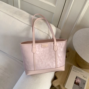 Gros plan du sac cabas rose avec logo doré sur un canapé blanc en lumière douce