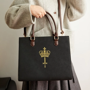 Detail of vintage black suede handbag with gold crown crest and brown leather straps