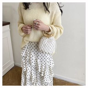 Detailed close-up of woven bucket bag with round wooden handles and stylish knit outfit