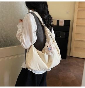 Detail of off-white canvas dumpling bag with adjustable strap and cute plush bunny charm