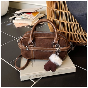 Detailed view of dark brown suede bowling bag with white contrast stitching and charm