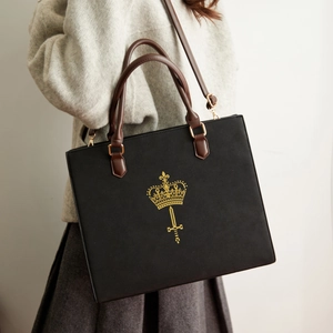 Detailed view of black tote bag with gold emblem and brown leather straps on a model