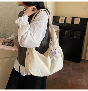 Detail of off-white hobo bag showing canvas texture, side zipper, and plush rabbit charm