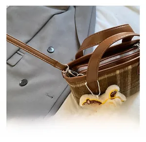Detail of plaid crossbody bag with brown leather strap and white plush rabbit charm