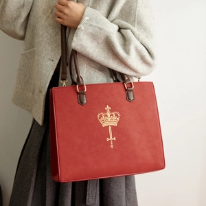 Detail view of burgundy suede tote with gold crown logo and premium leather handle