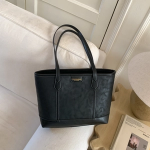 Détail du grand sac cabas noir en cuir grainé avec logo doré sur un canapé blanc