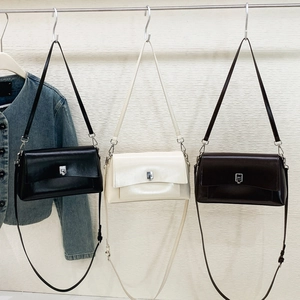 Three minimalist glossy leather flap bags in black, beige, and dark coffee on display