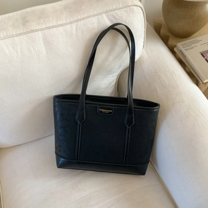 Détail du sac cabas en cuir noir avec logo en métal posé sur un canapé accueillant