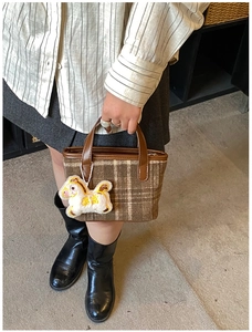 Detail of brown plaid tote bag with wool texture, leather handles and cute plush charm
