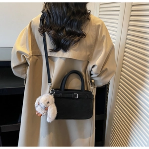 Detail einer schwarzen eckigen Umhängetasche mit Plüschhasen-Anhänger am Trenchcoat