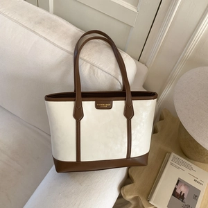 Détail d'un sac cabas beige vintage avec anses marron posé sur un canapé confortable