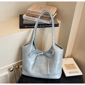 Detail of light blue faux leather tote bag featuring a bow decoration and embossed texture