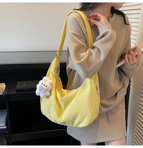 Detail view of bright yellow crescent bag with silver zipper and white plush bear charm