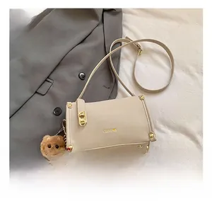 Detail of off-white leather square bag with gold hardware and plush bear accessory