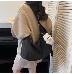 Detail of a black nylon crescent crossbody bag styled with a cute white bunny pendant