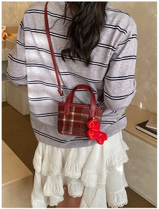 Detail of red checkered crossbody bag with cute puppy charm worn by a model
