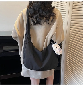 Detailed view of black nylon crescent crossbody bag with white plush bear pendant