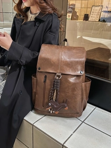 Brown vintage leather backpack with dachshund charm on black coat background