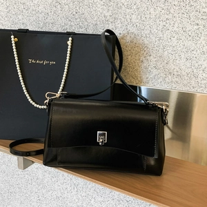 Close-up of black glossy square bag featuring a silver twist lock on a wooden shelf