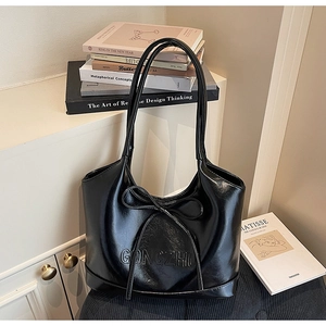 Detail of glossy black tote bag with long bow decoration and embossed brand logo