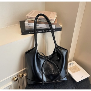 Detail of black glossy tote bag featuring a bow tie and embossed GONGZHU lettering