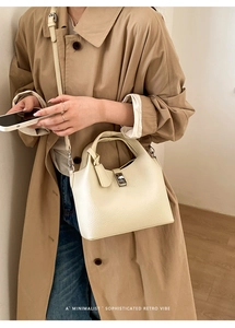 Detail of minimalist cream leather bucket bag showing lychee grain texture and metal buckle
